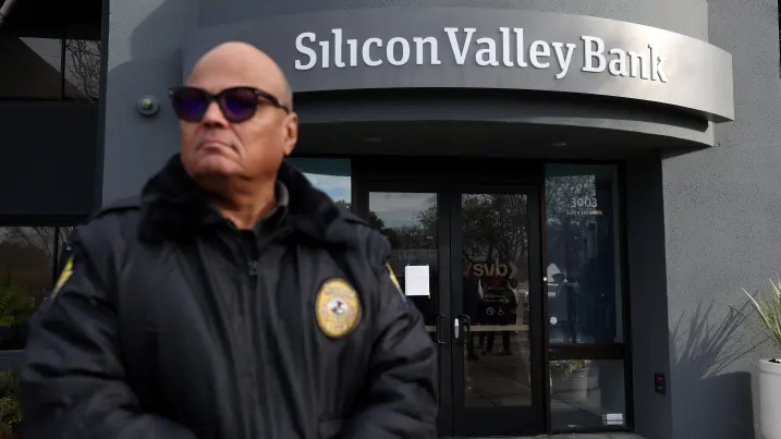 A security guard at Silicon Valley Bank monitors a line of people outside the office on March 13, 2023 in Santa Clara, California.
